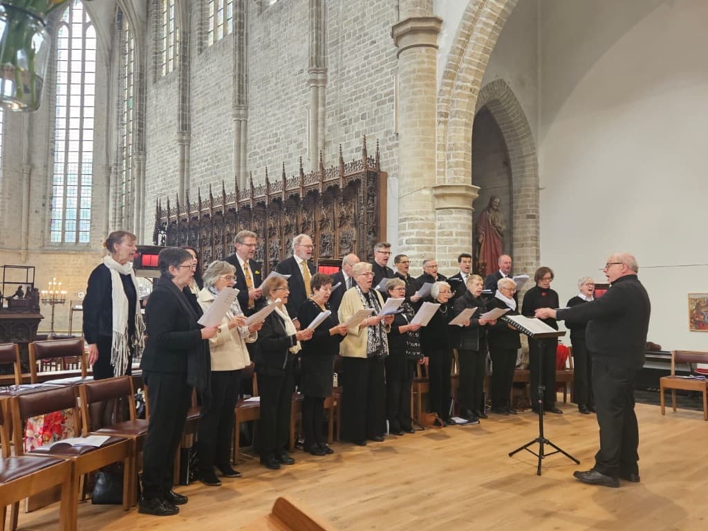 Het Gertro-koor tijdens een repetitie in de Sint-Geertruikerk, met hoofddirigent Jan Breuls en koorleden voor het gotische doksaal.